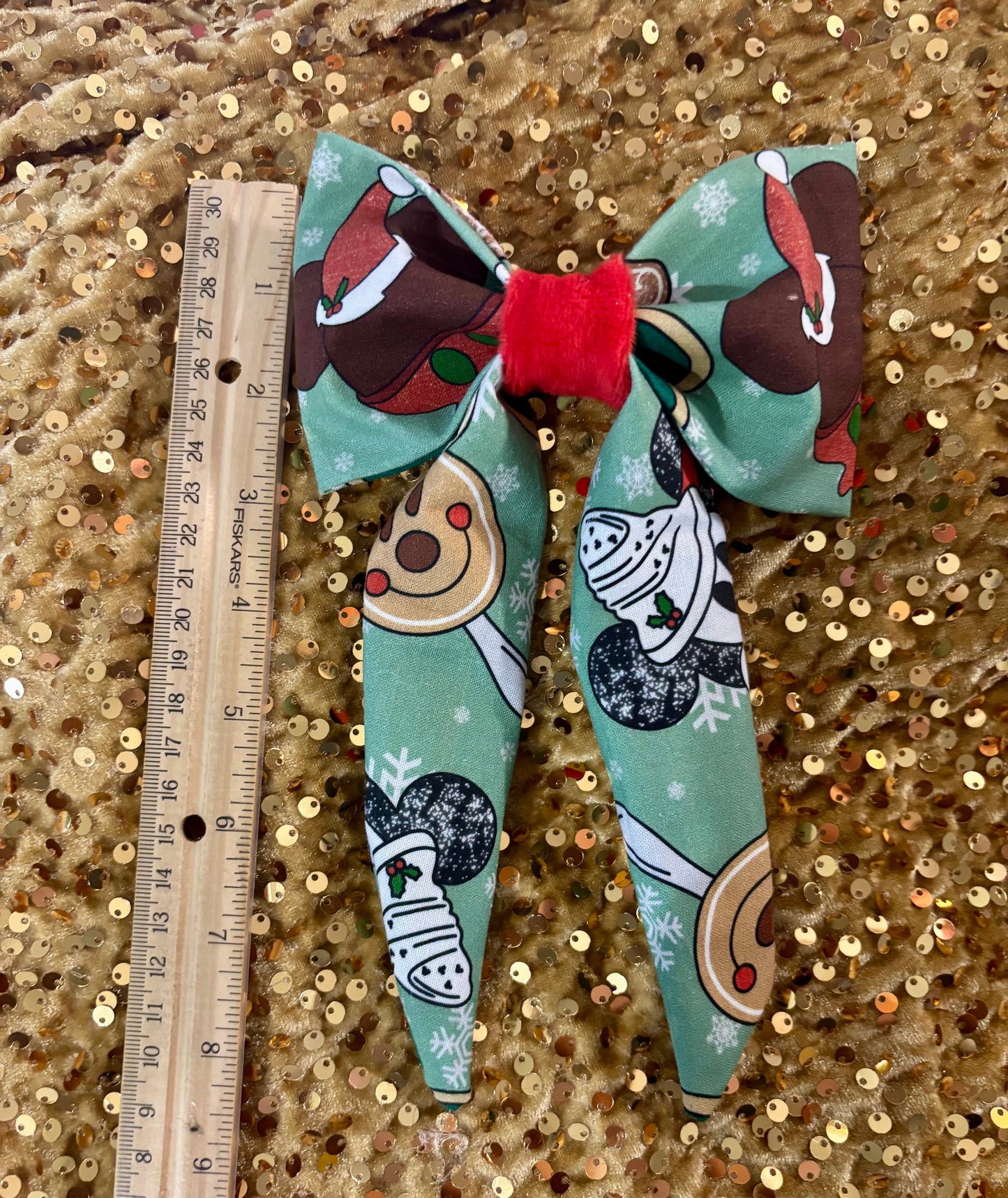 Decorative hair bow with cartoon characters on a gold sequin background, accompanied by a ruler for scale.