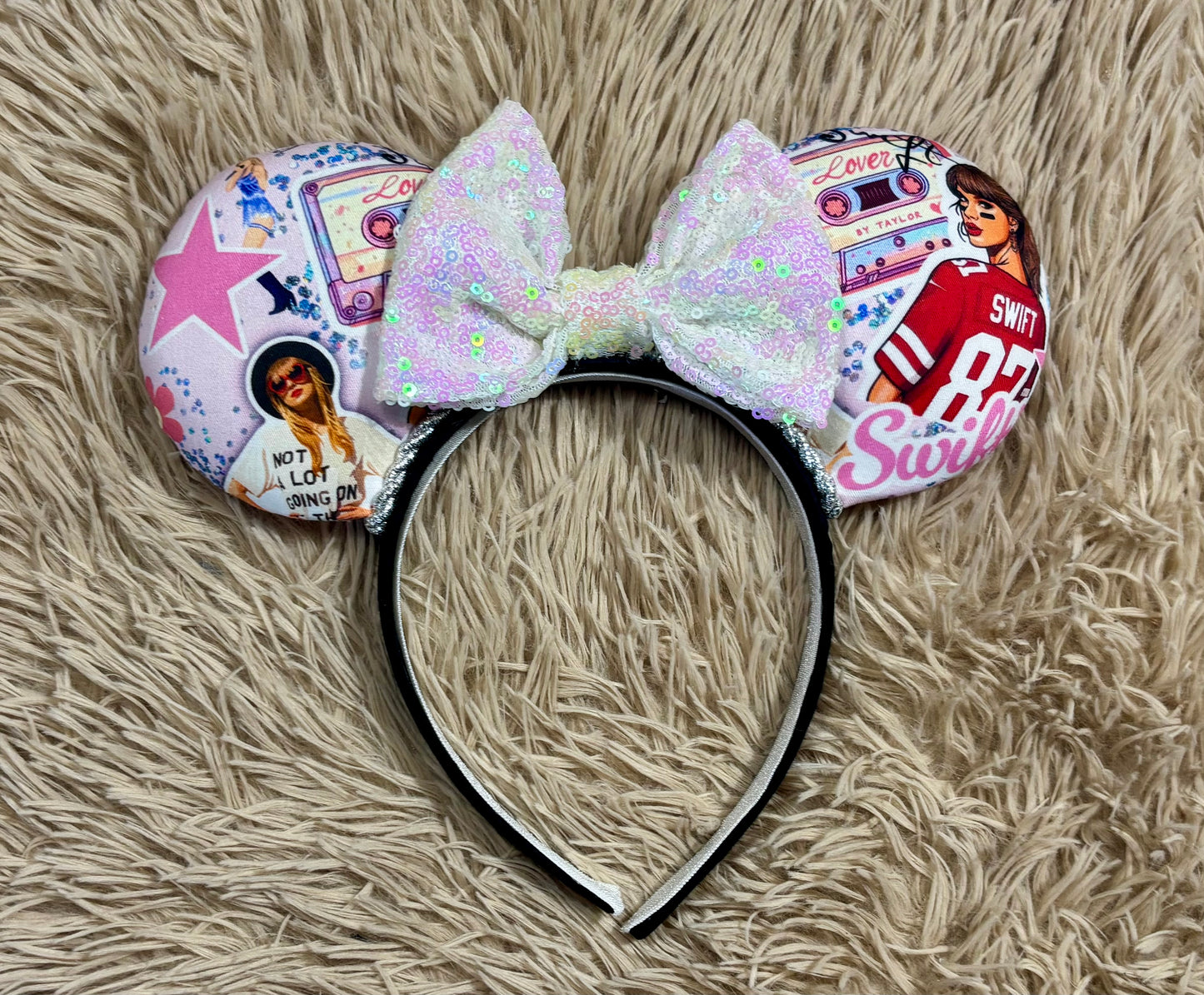An ear headband with a large iridescent bow and custom printed ears featuring retro cassette graphics, a pink star, and a portrait of singer.