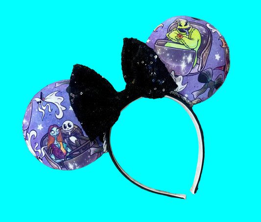 An ear headband featuring a black sequined bow and purple printed ears with characters from NBC, displayed on a teal background.