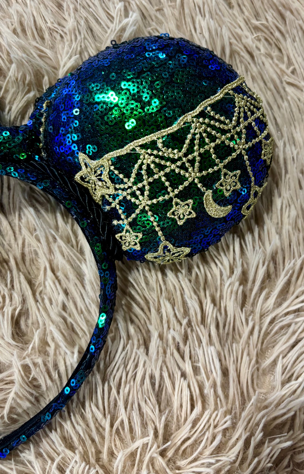 A pair of blue and green iridescent ear headband featuring dark blue and green sequins with gold embroidered stars, moons, and web patterns.