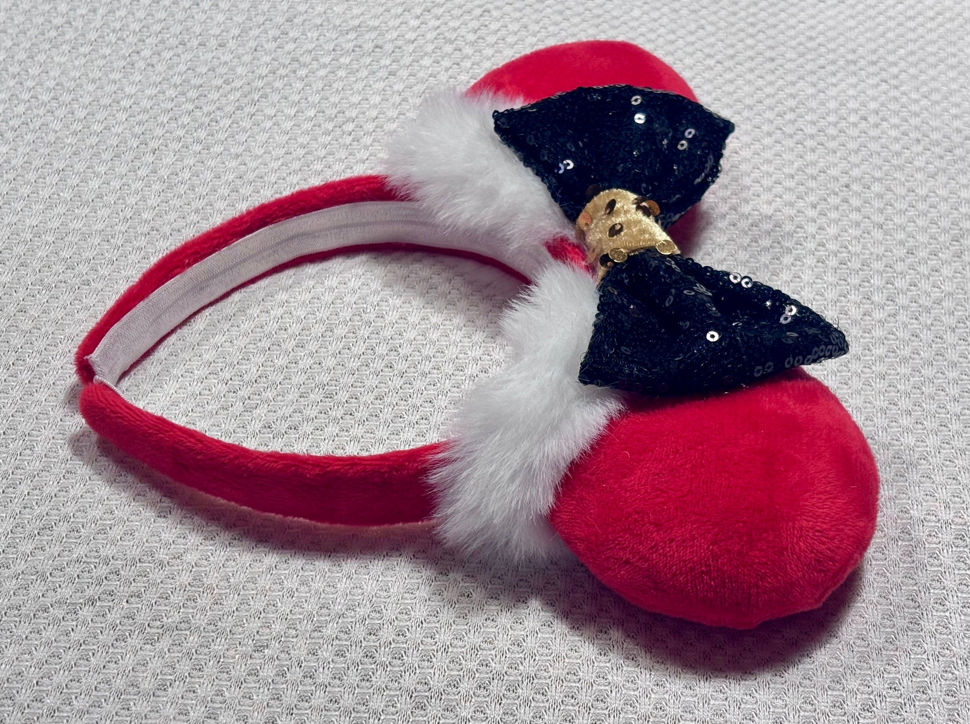 Minnie Mouse ears headband with red plush ears and black bow with gold middle and fluffy white trim on a white background