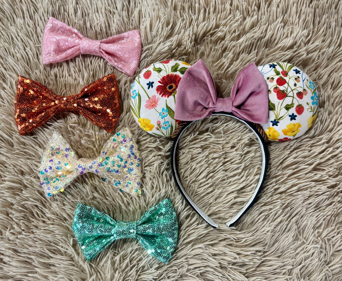An ear headband accessory featuring a floral-themed print on the ears and a pink velvet bow in the center with copper colored twisted trim along the inner ears. Shown with bow color options in case you don't want the velvet pink one.