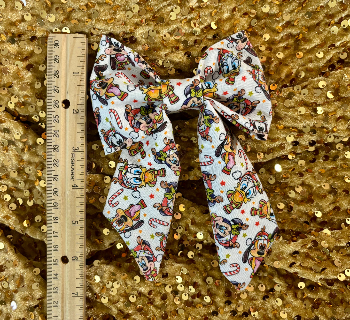 Large decorative bow with cartoon character pattern on a gold sequin background, accompanied by a ruler for scale.