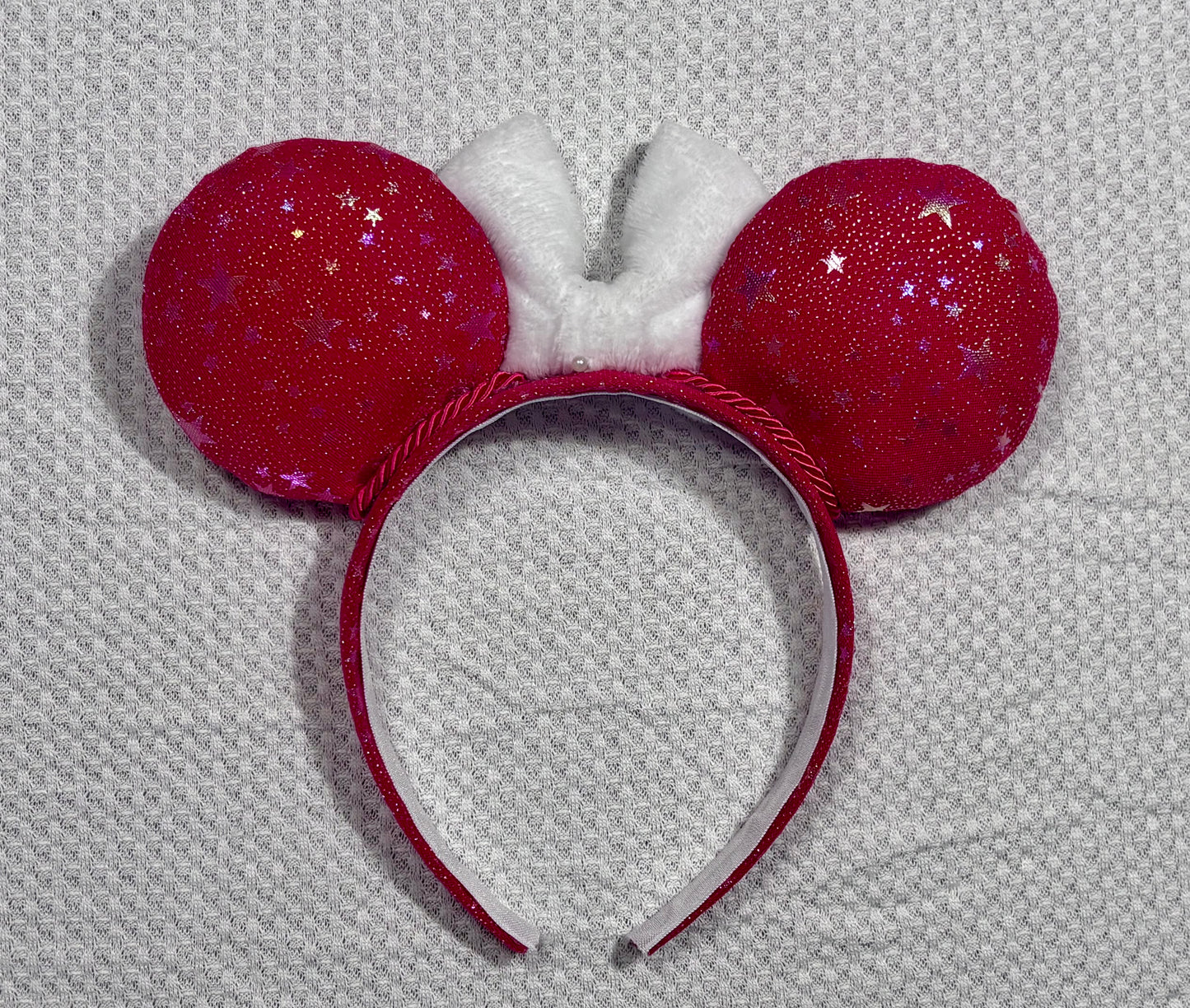 Handmade and ready to ship red mouse ears with iridescent stars on both the front and back along with the headband as well. The set has a white soft bow. Item is shown on a white background. The back side of the mouse ears is shown with the same fabric as the front.
