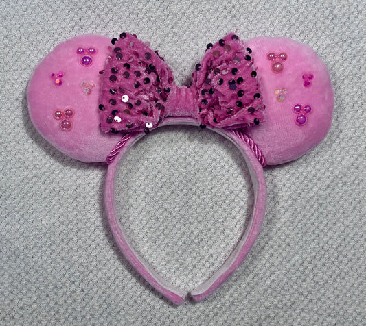 Pink mouse ears headband with decorative bow and embellishments on a gray background
