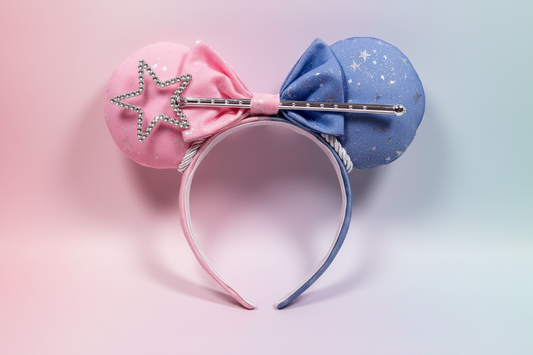 Colorful mouse ear headband with pink one one side and blue on the other with a bow the same and it includes a wand in the bow. Shown on a gradient background