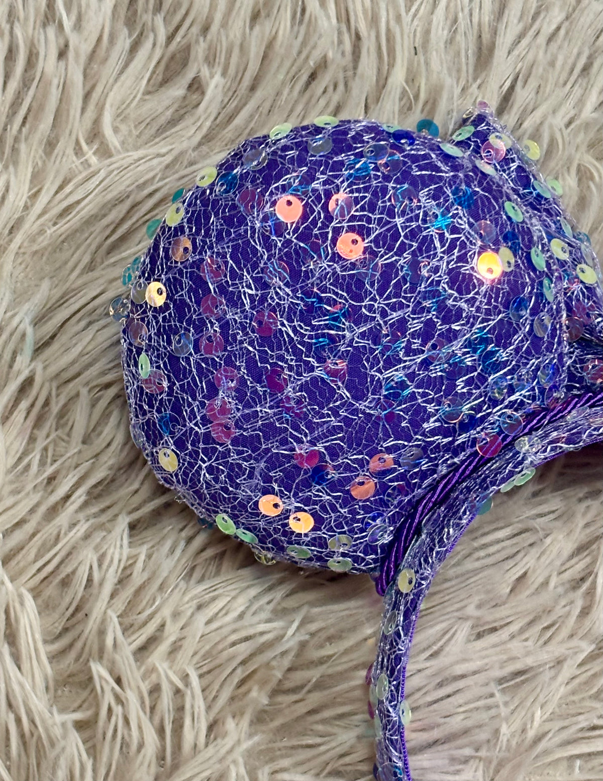 A close up of the purple iridescent sequined headband and purple twisted trim along the inner ear.