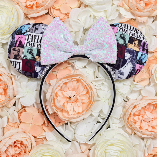 multicolor collage print on the ears and a sparkling iridescent white sequin bow on top, displayed on a bed of peach and white faux flowers.