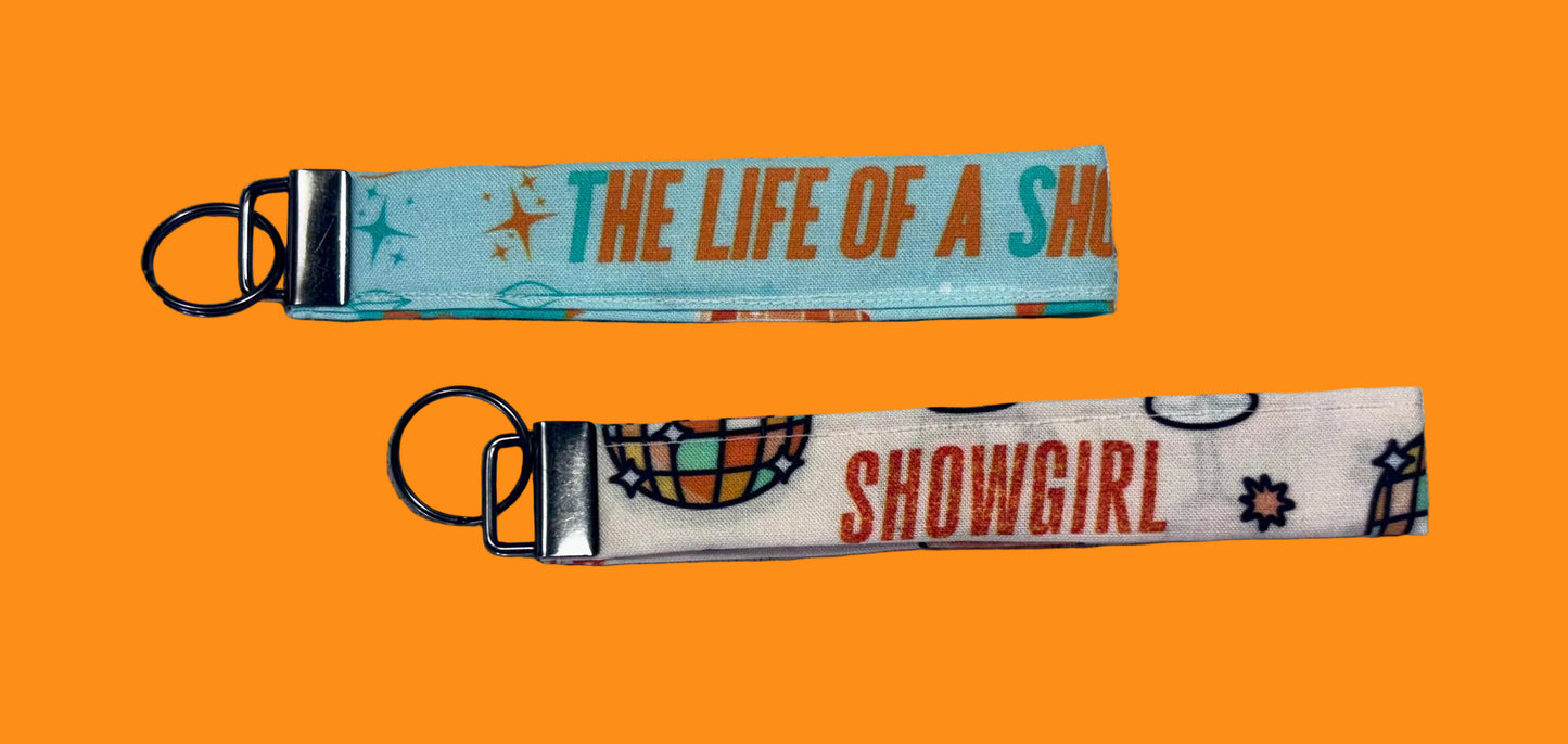 Two keychains with 'The Life of a Showgirl' text on a textured white background