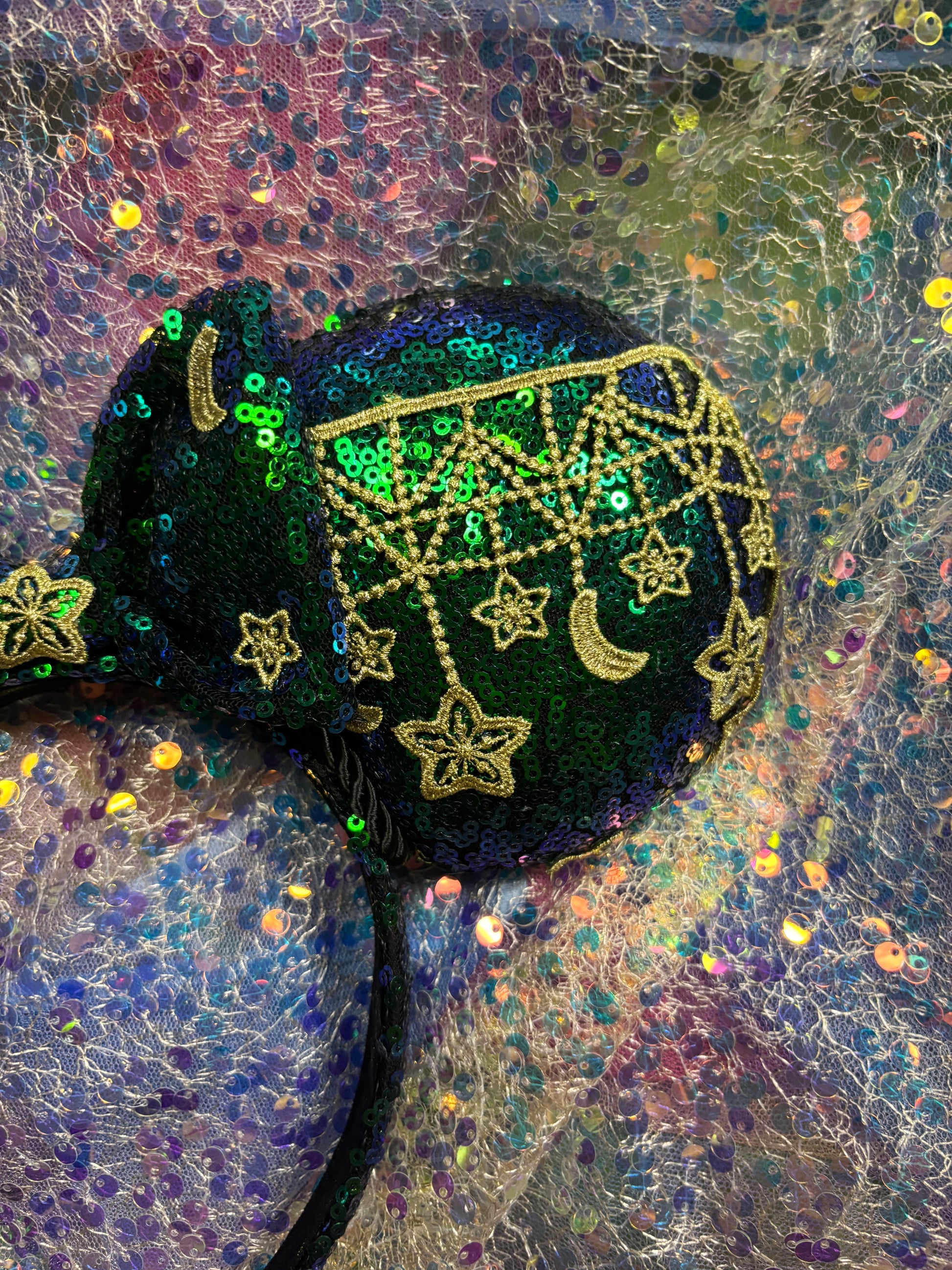 Mouse Ear headband that is a Handmade Iridescent blue and green sequins with gold sun, moon and stars attached to them. bow with star and moon patterns on a glittery background.