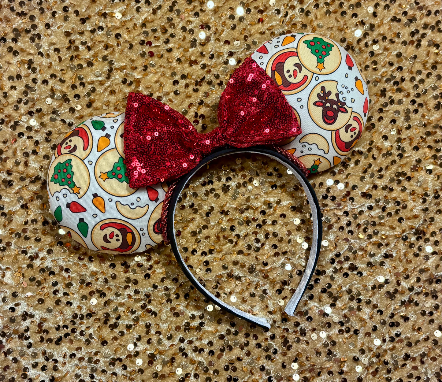 Christmas Sugar Cookie mouse ears with the fabric on both the front and back. The headband is black universal sized and fits most. The set has a red sequin bow. Item is shown on a gold sequin background