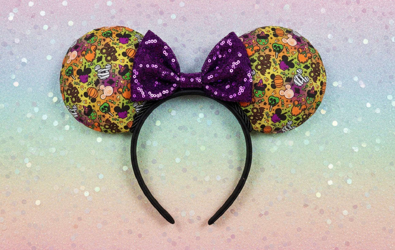 Colorful Halloween-themed mouse ears with park snacks on the mouse ears with a sequin purple bow on a black on a light backgroundeadband with black twisted trim.