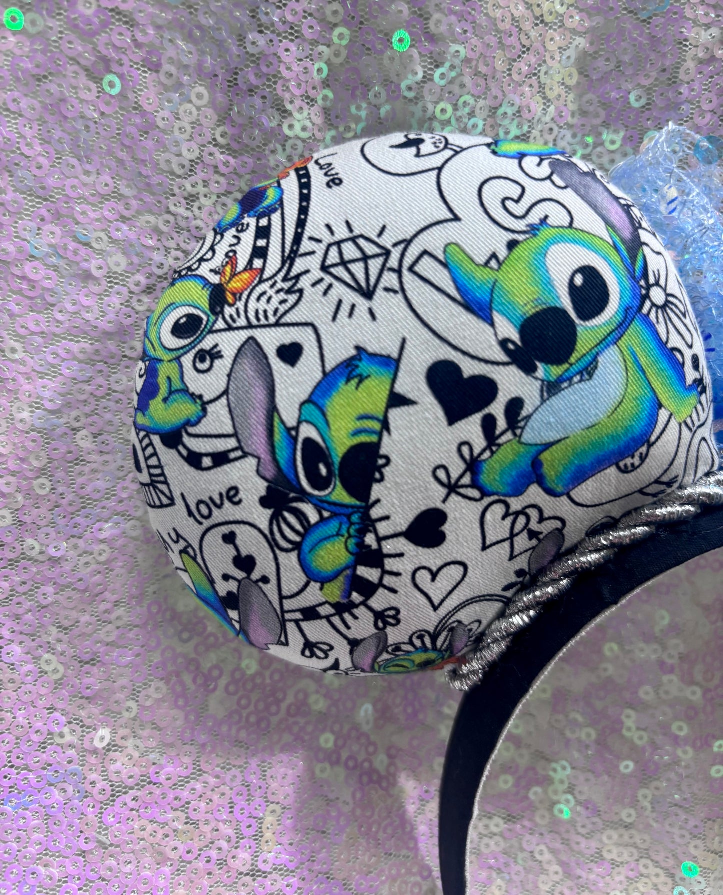 Back left ear view. Handmade and ready to ship Mouse ears with Stitch cartoon character design on the fabric with silver twisted trim on a black universal sized headband and a blue sequin bow.