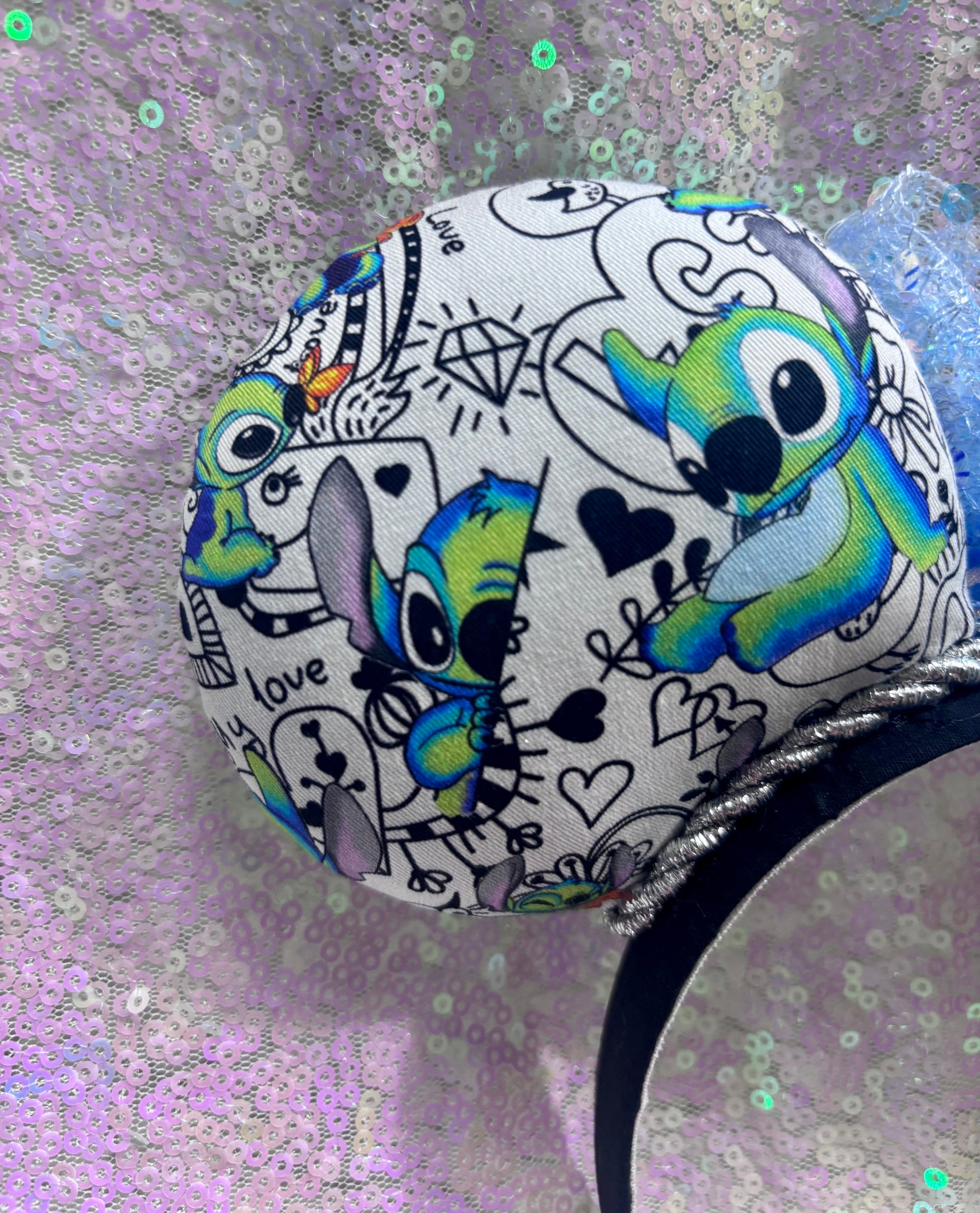 Back left ear view. Handmade and ready to ship Mouse ears with Stitch cartoon character design on the fabric with silver twisted trim on a black universal sized headband and a blue sequin bow.