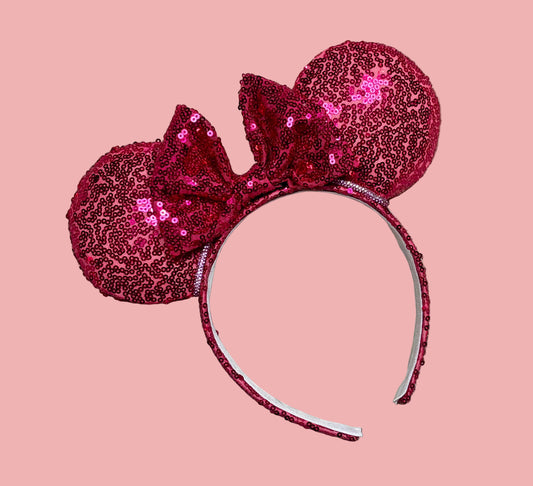 A pair of pink sequined ears on a universal sized headband with white elastic lining and a rhinestone trim along the inner ears. 