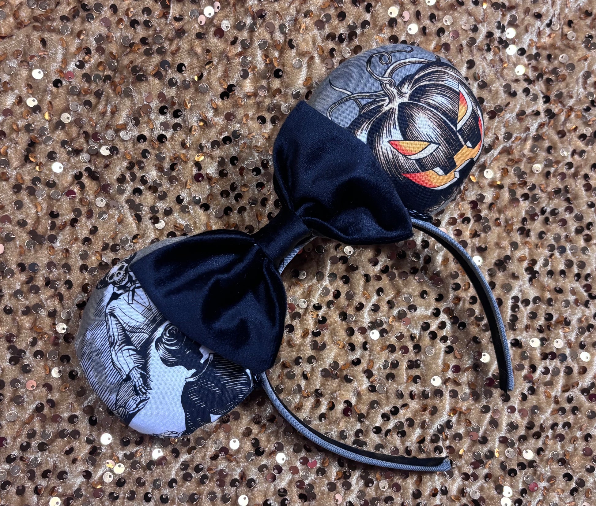 Handmade and one of a kind Halloween mouse ears with the fabric on both the front and back. Skeleton ghost having a seance on one side and an evil pumpkin on the other ear. The headband is grey and universal sized and fits most. The set has a black velvet bow. Item is shown on a gold sequin background.