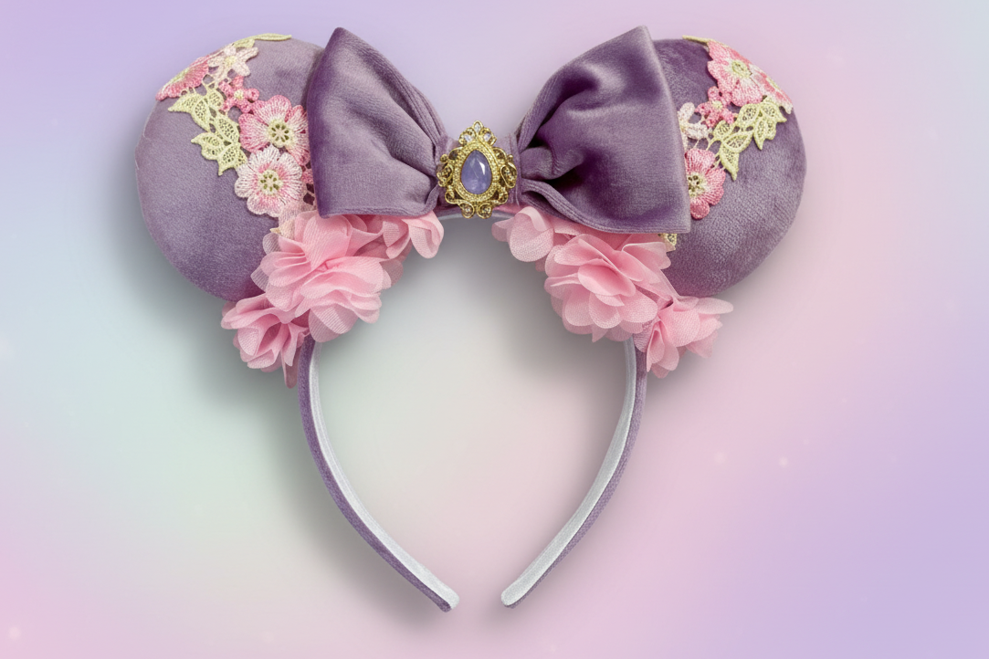 Decorative mouse ears inspired by Rapunzel. The headband and ears have floral details and a bow with a purple gem in the middle. Floral trim as well. Shown on a pastel background