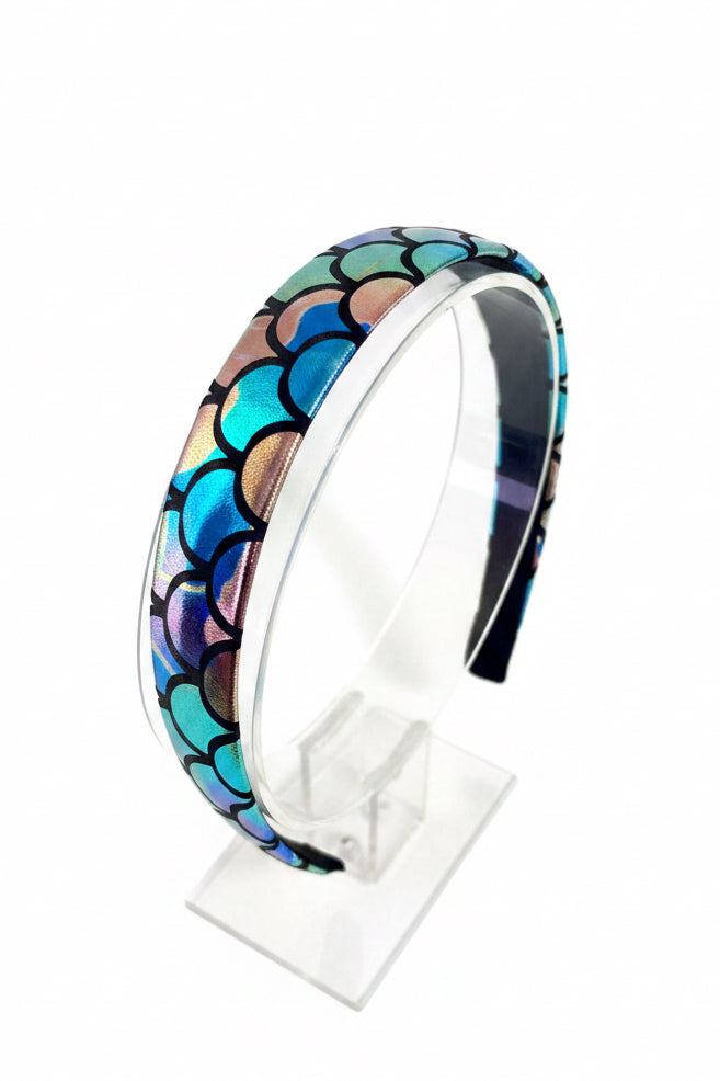 Multicolored rainbow scale headband on a white stand with a white background.