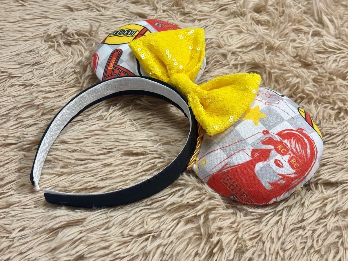 An ear headband featuring a bright yellow sequined bow. The set has TS and Chiefs images on it. Set on a universal sized headband.