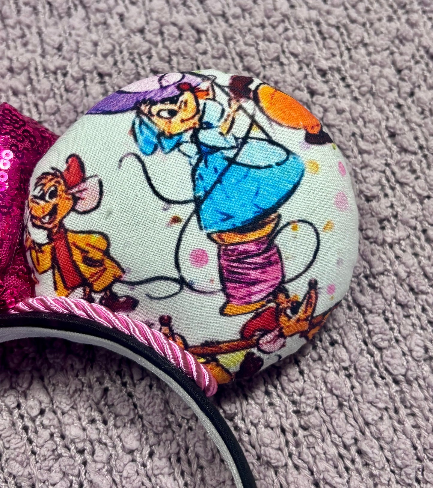 Close up of back side of mouse ear. Handmade and ready to ship Sewing Mice mouse ears with the fabric on both the front and back. The headband is black universal sized and fits most. The set has a hot pink sequin bow with pink twisted trim along the inner mouse ears. Item is shown on a lavender fluffy background.