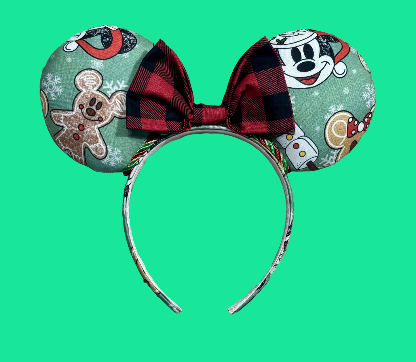 A pair of Christmas themed mouse ears headband featuring a festive holiday print with gingerbread men, snowflakes, and a red plaid bow.