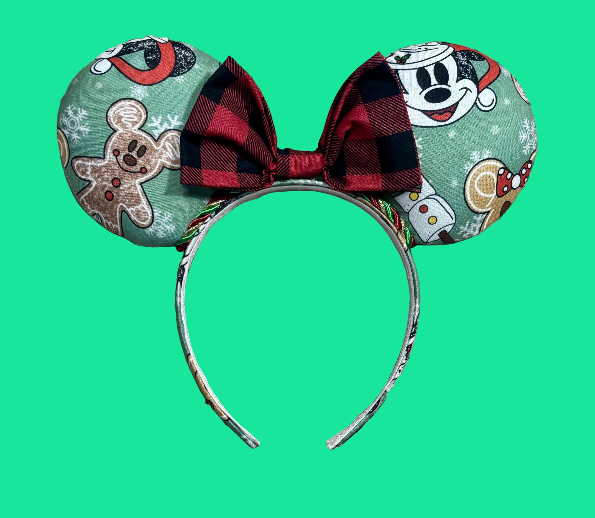 A pair of Christmas themed mouse ears headband featuring a festive holiday print with gingerbread men, snowflakes, and a red plaid bow.
