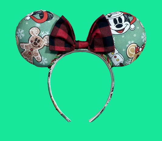A pair of Christmas themed mouse ears headband featuring a festive holiday print with gingerbread men, snowflakes, and a red plaid bow.