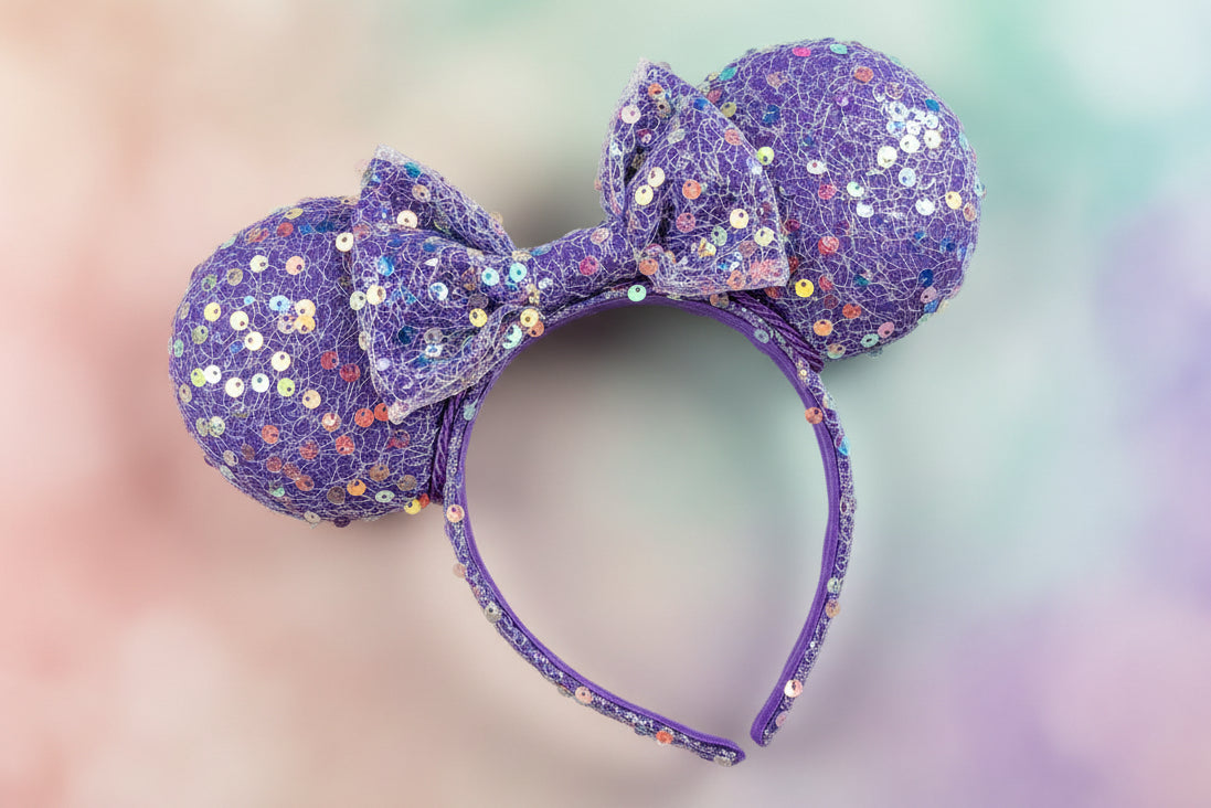 Purple sequin mouse ears on the ears, headband and bow. Purple twisted trim along inner ears. Shown on a blurred multicolored background