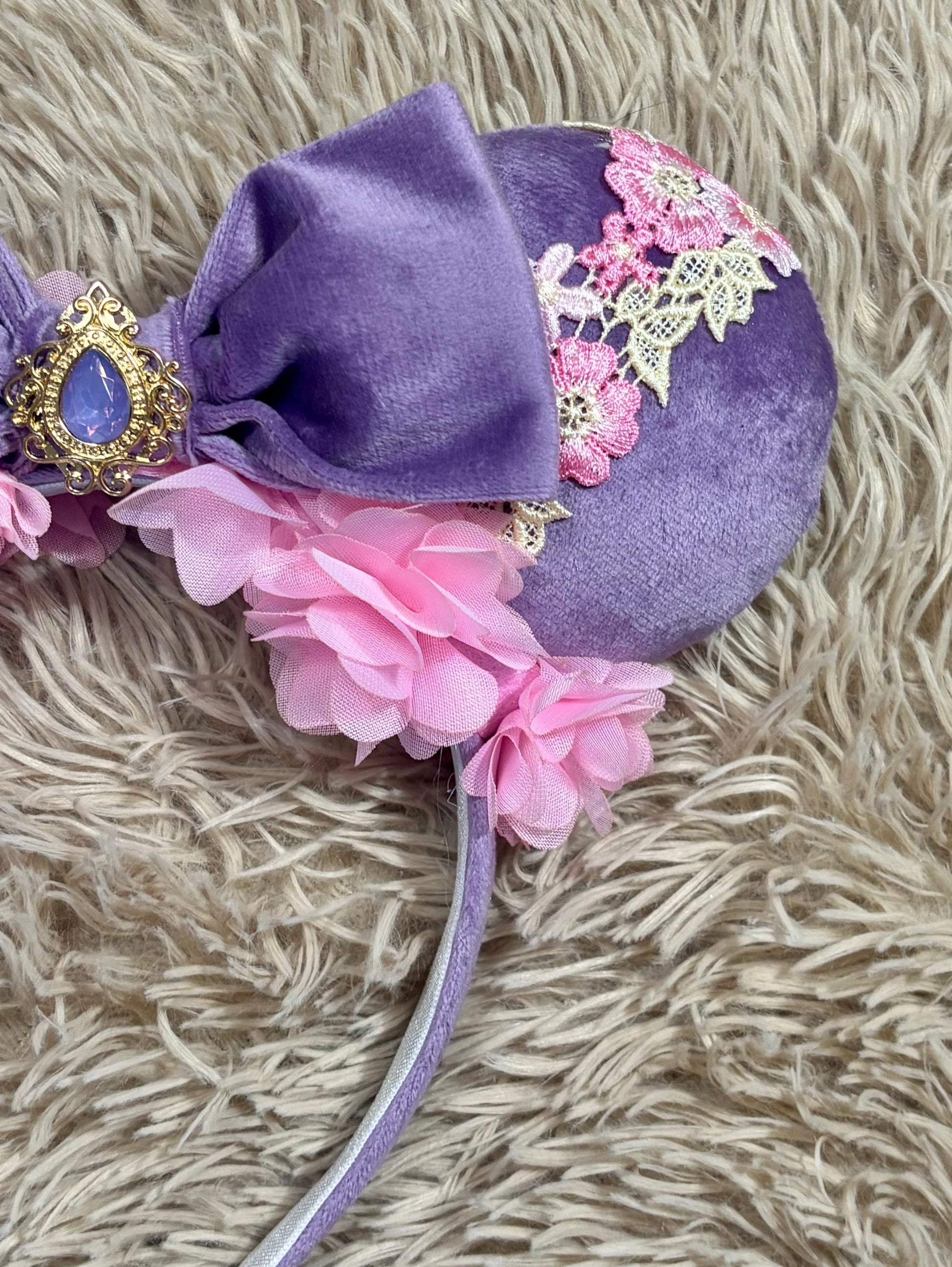 Purple and pink fabric mouse ears headband with a large velvet bow, floral lace appliques, and a purple gem accent.