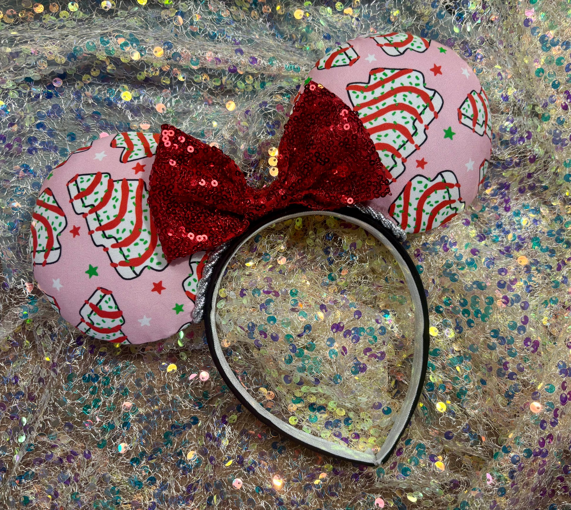 Pink minnie mouse ears with a red bow on a glittery background.