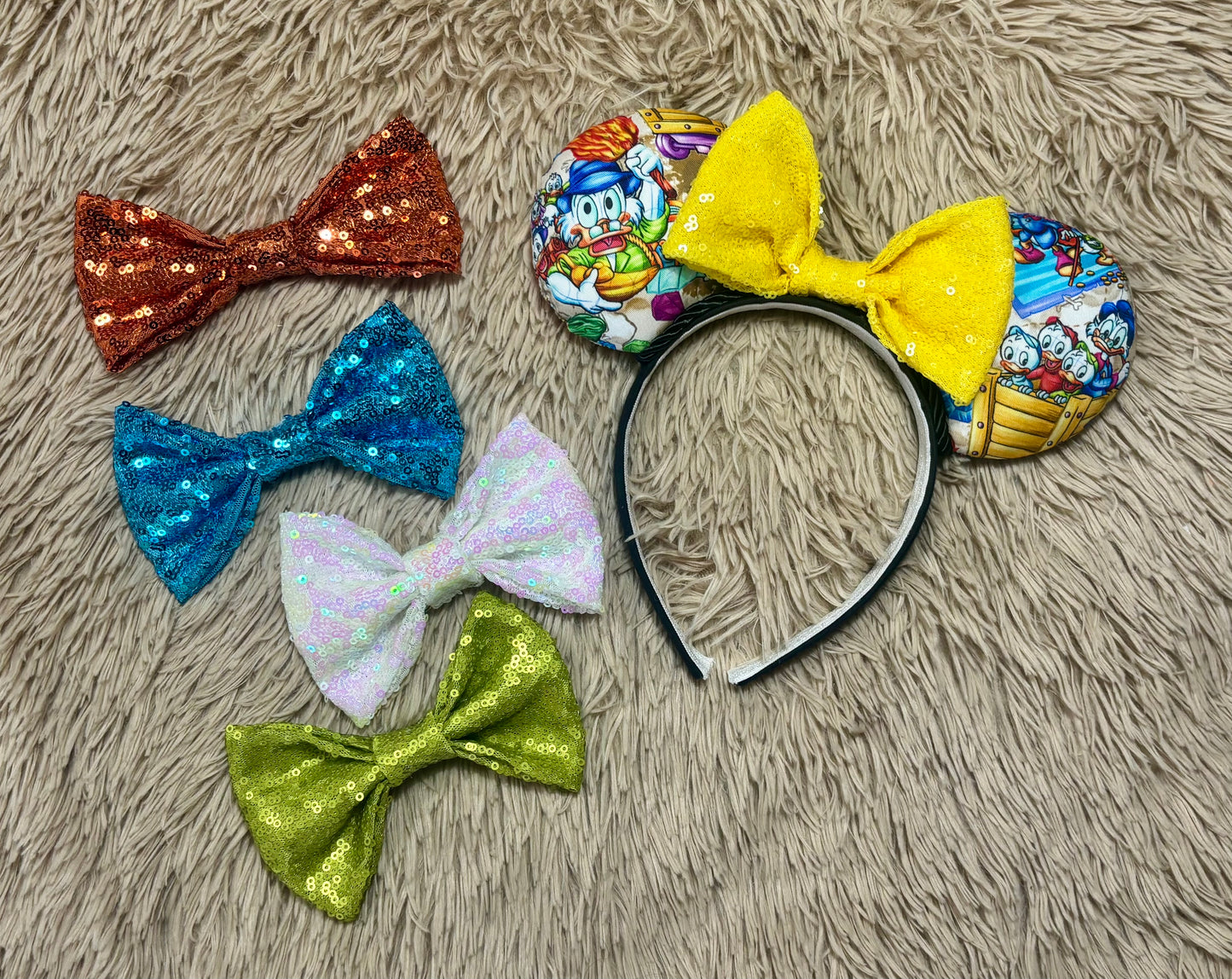 A headband featuring a colorful cartoon print of famous cartoon Duck characters, accented by a large yellow sequined bow in the center. Shown with other bow color choices in case you don't want the default yellow sequin bow. 
