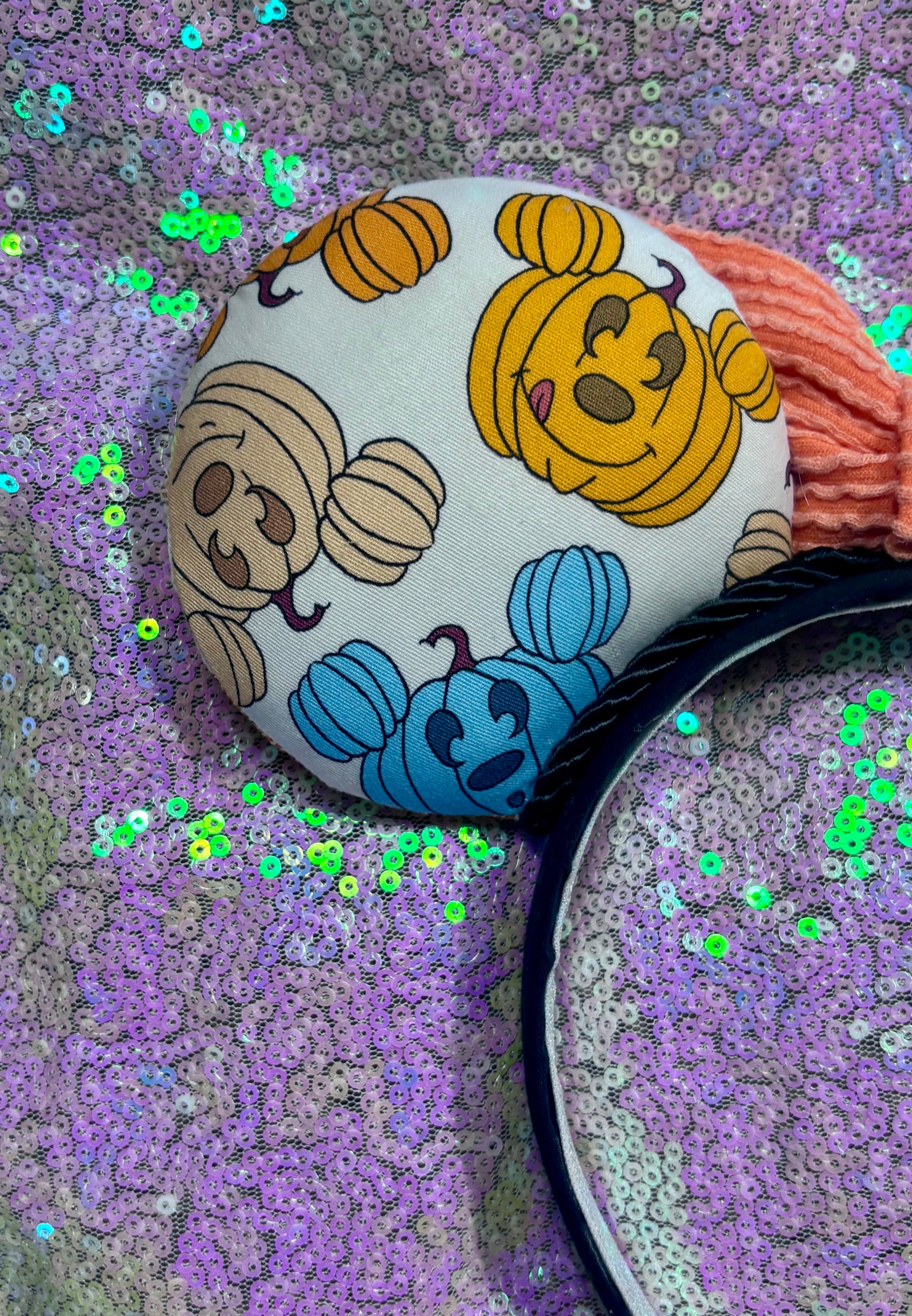 Mouse Ears with pumpkins on them on a black headband with an orange waffle print bow and glitter background.