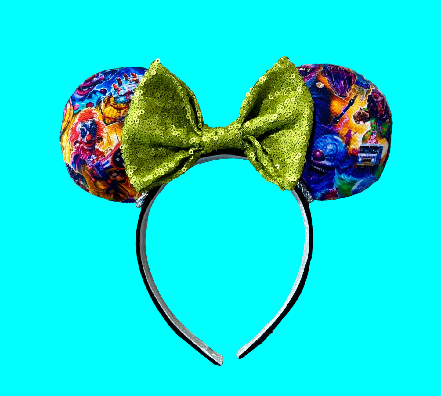 A pair of ear headband featuring a vibrant multicolor abstract patterned fabric and a prominent sequined lime green bow.