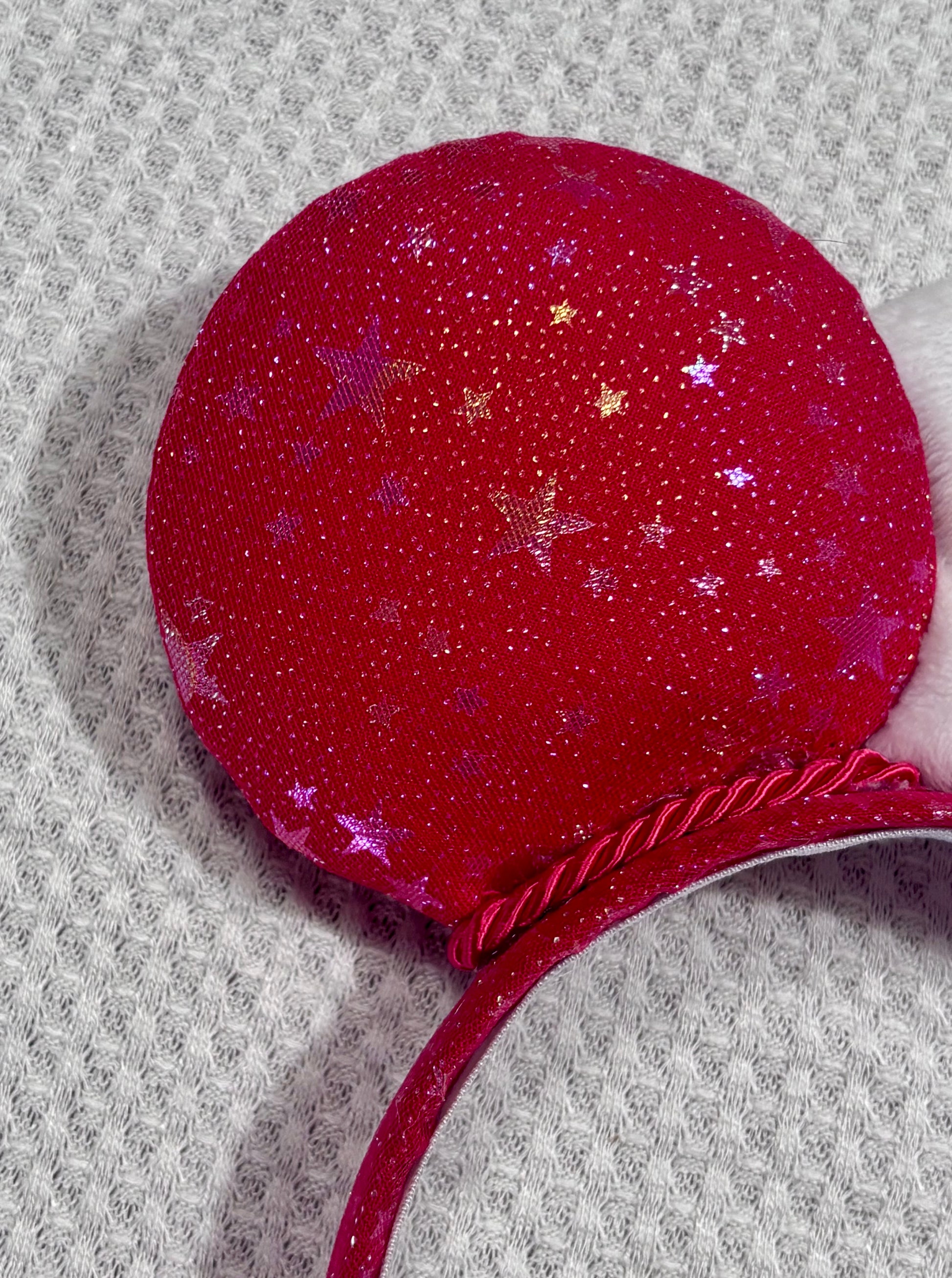 Handmade and ready to ship red mouse ears with iridescent stars on both the front and back along with the headband as well. The set has a white soft bow. Item is shown on a white background.