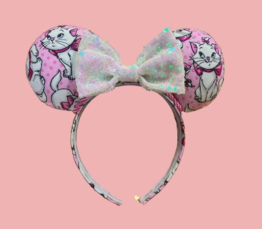 Handmade and ready to ship Marie Inspired Mouse ears with images of her on the front and back of mouse ears shown with a white iridescent sequin bow. The headband has a matching Marie poly cotton fabric and is a universal sized headband.