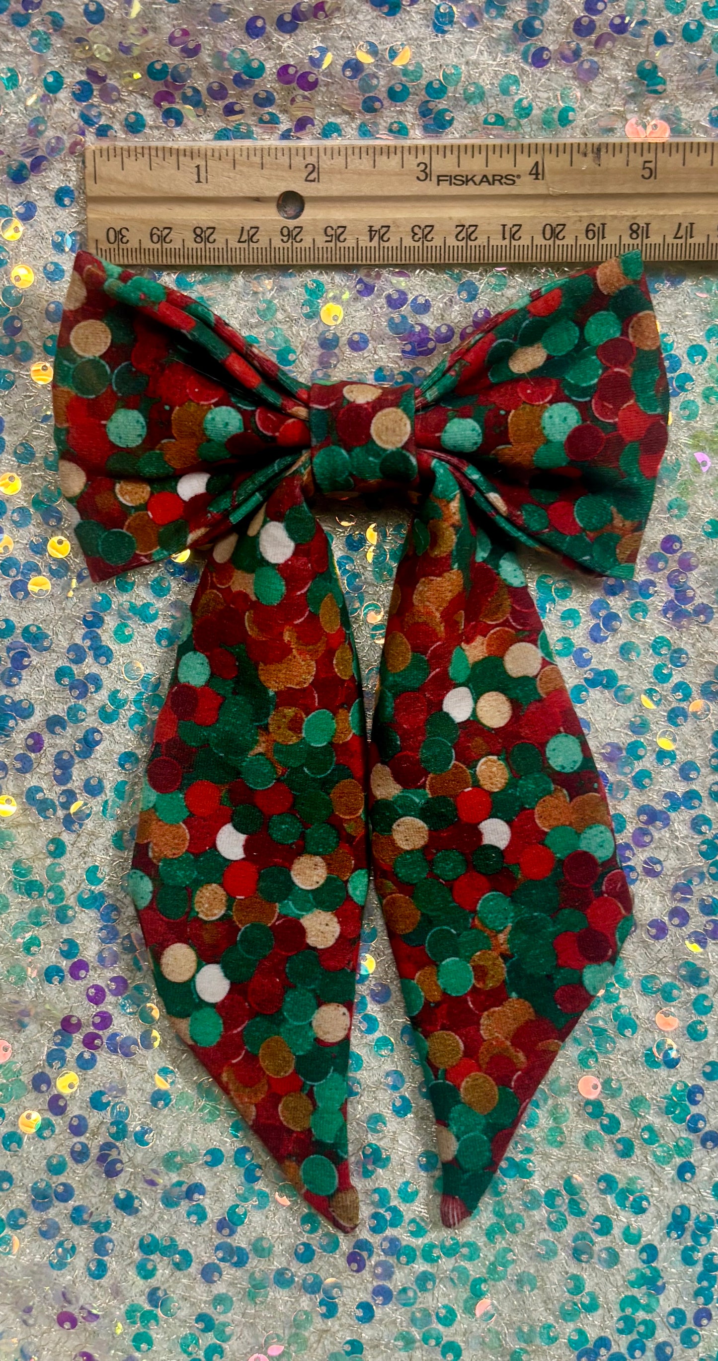 Christmas colors dot bow with a ruler for scale on a glittery background.
