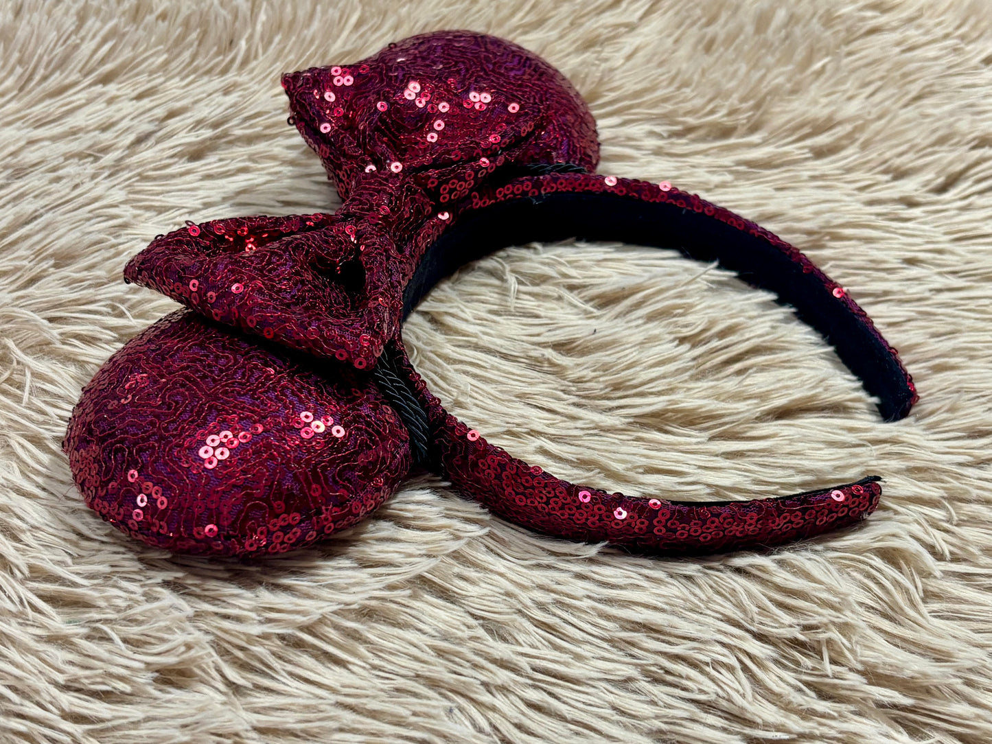 A pair of sequined ears headband with a bow, featuring deep magenta sequins on a black headband.