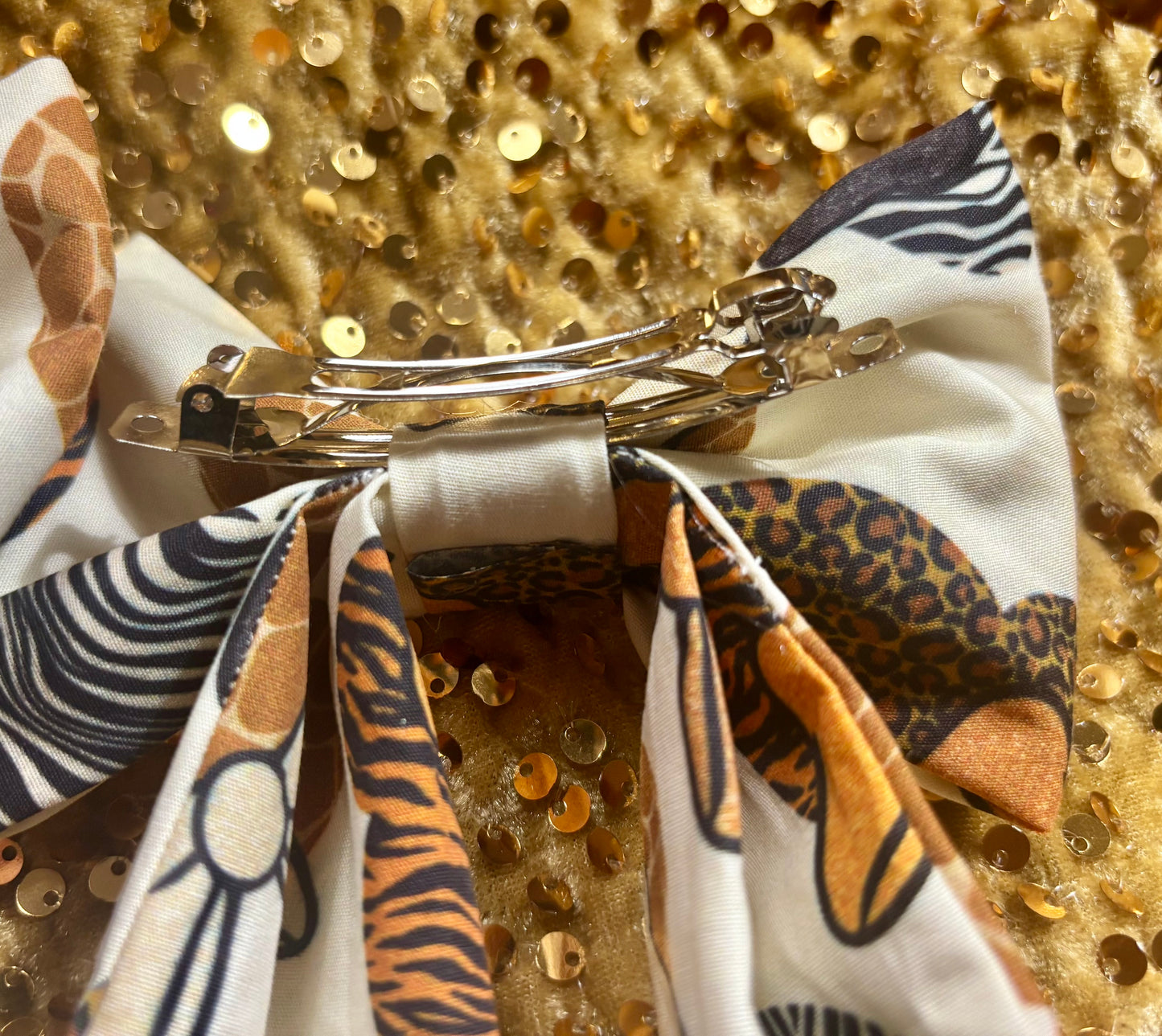 Metallic hair clip with patterned ribbons on a glittery gold background