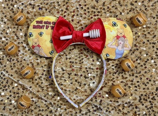 Pooh and Taylor mashup Honey Mouse ears with a soft plus red bow with a honeycomb in the middle of bow. Shown on a glittery gold background
