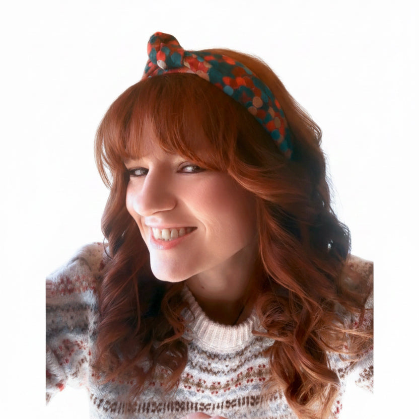 Woman with red hair wearing a Christmas colored patterned headband on a white background