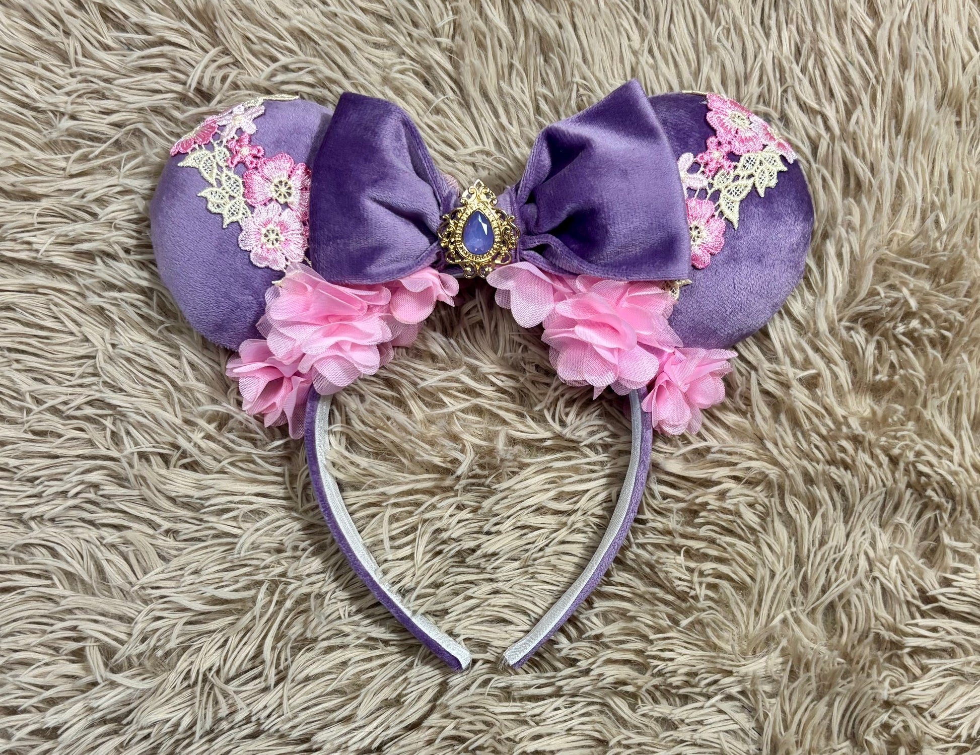 Purple and pink fabric mouse ears headband with a large velvet bow, floral lace appliques, and a purple gem accent.