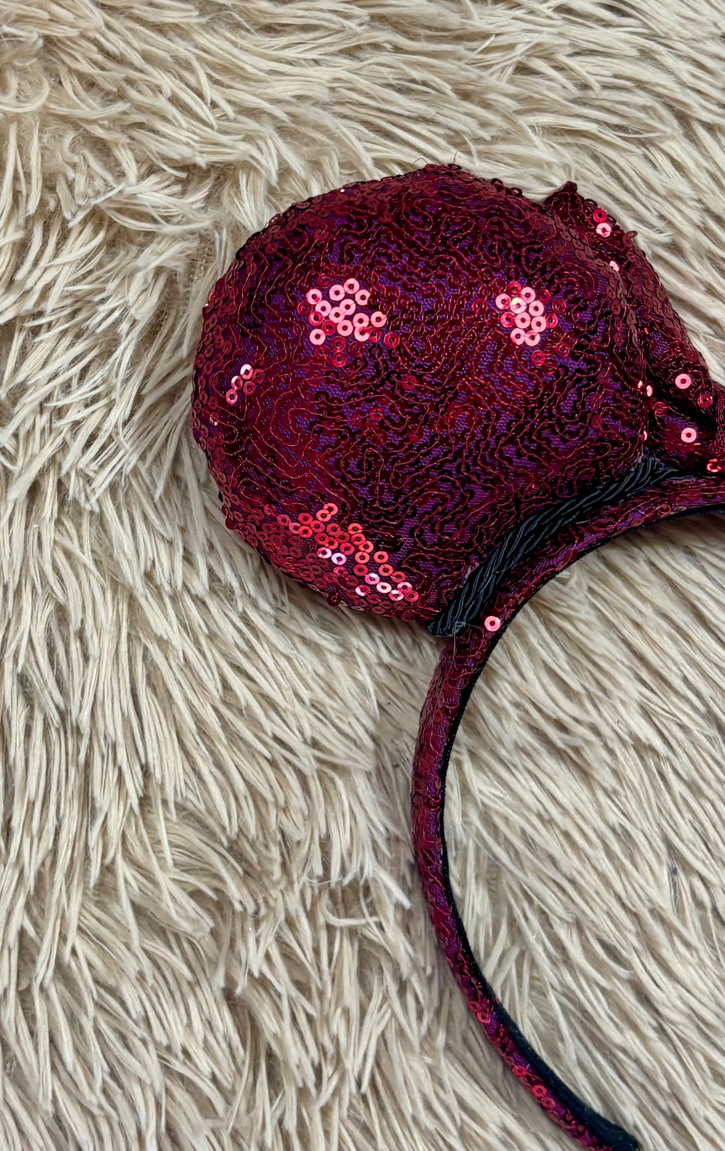 A pair of sequined ears headband with a bow, featuring deep magenta sequins on a black headband.
