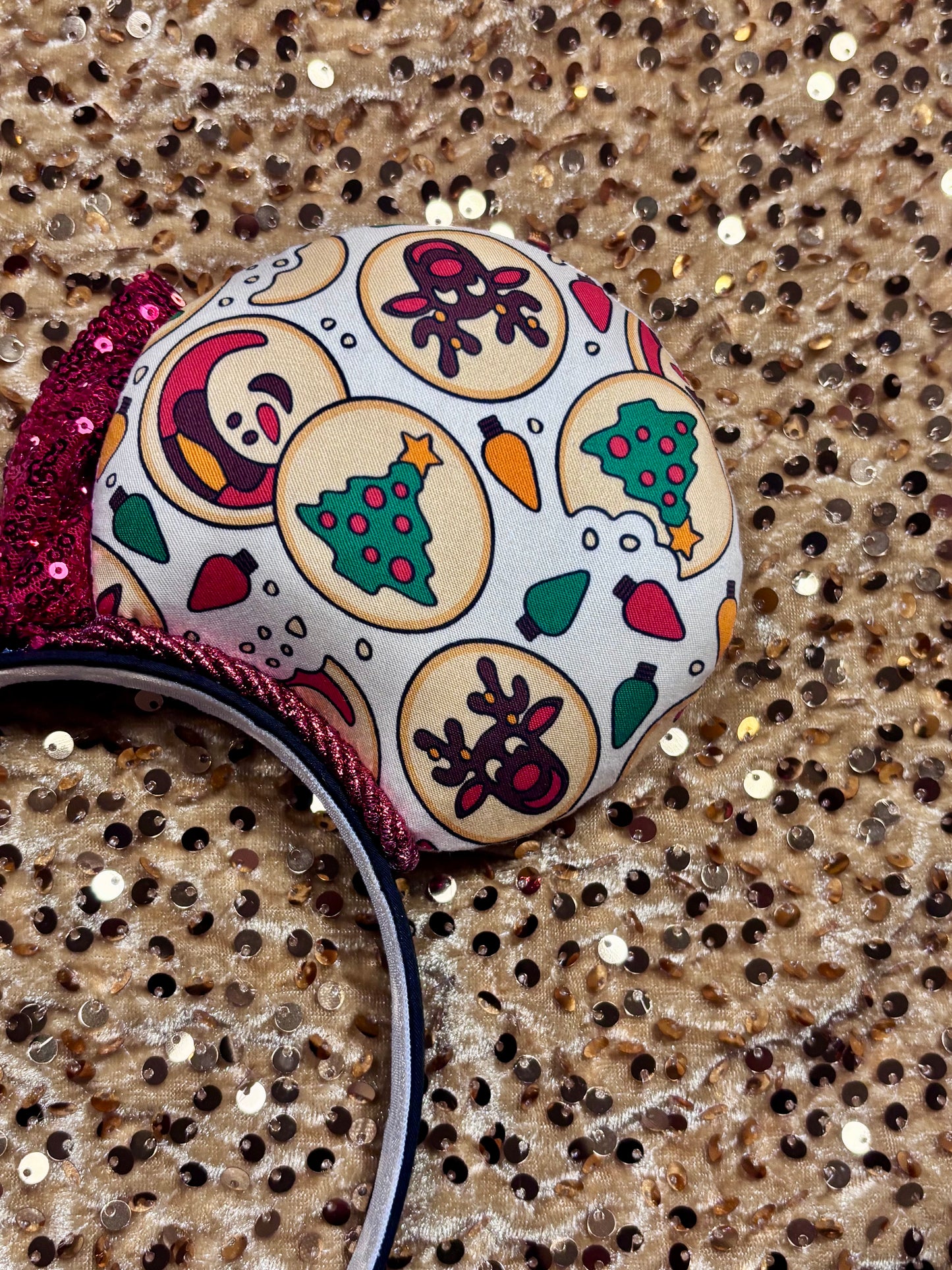 Christmas Sugar Cookie mouse ears with the fabric on both the front and back. The headband is black universal sized and fits most. The set has a red sequin bow. Item is shown on a gold sequin background