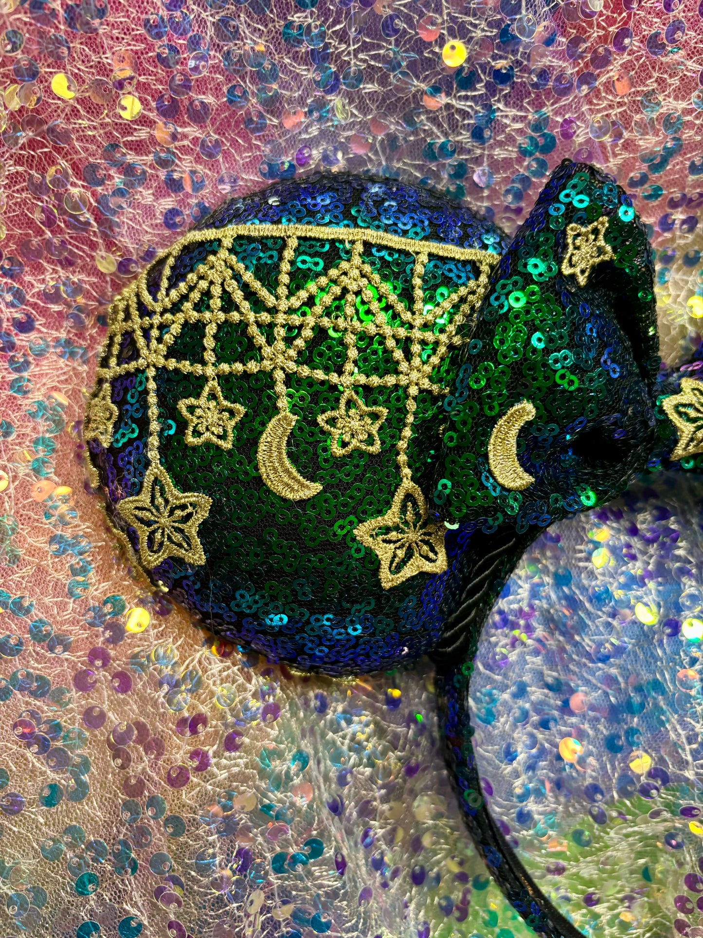 Mouse Ear headband that is a Handmade Iridescent blue and green sequins with gold sun, moon and stars attached to them. bow with star and moon patterns on a glittery background