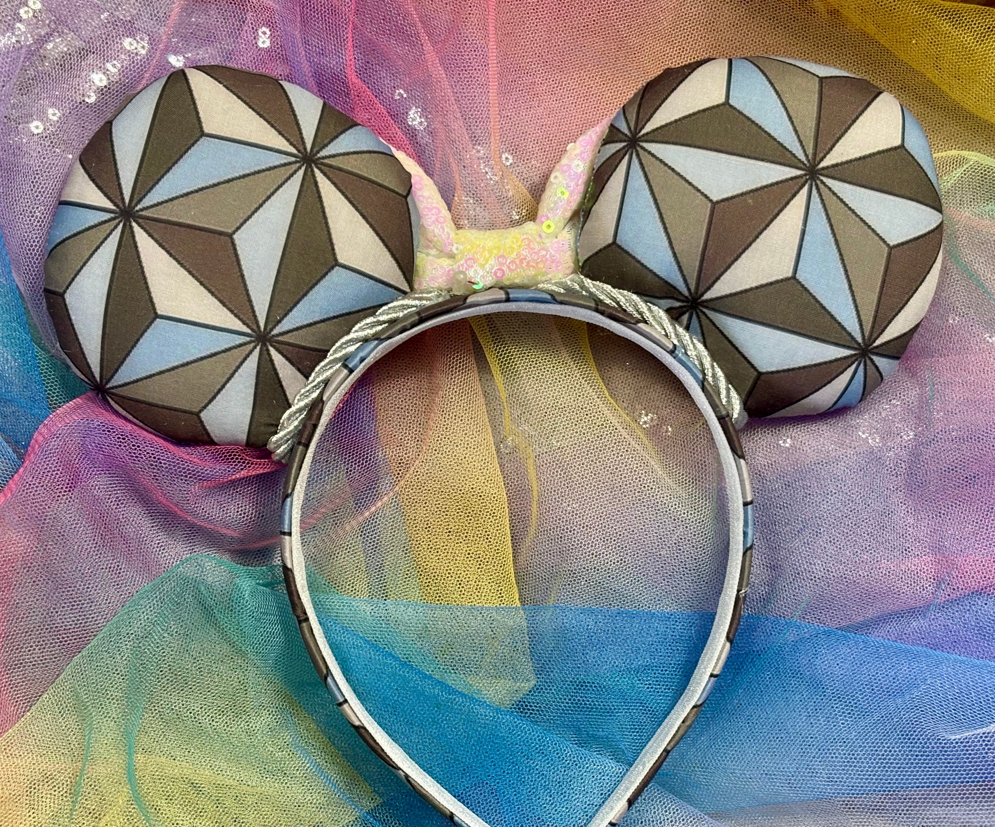 Mouse ear headband with a geometric design inspired by Spaceship Earth ride and a white iridescent bow on a colorful background. Back view of the mouse ears.