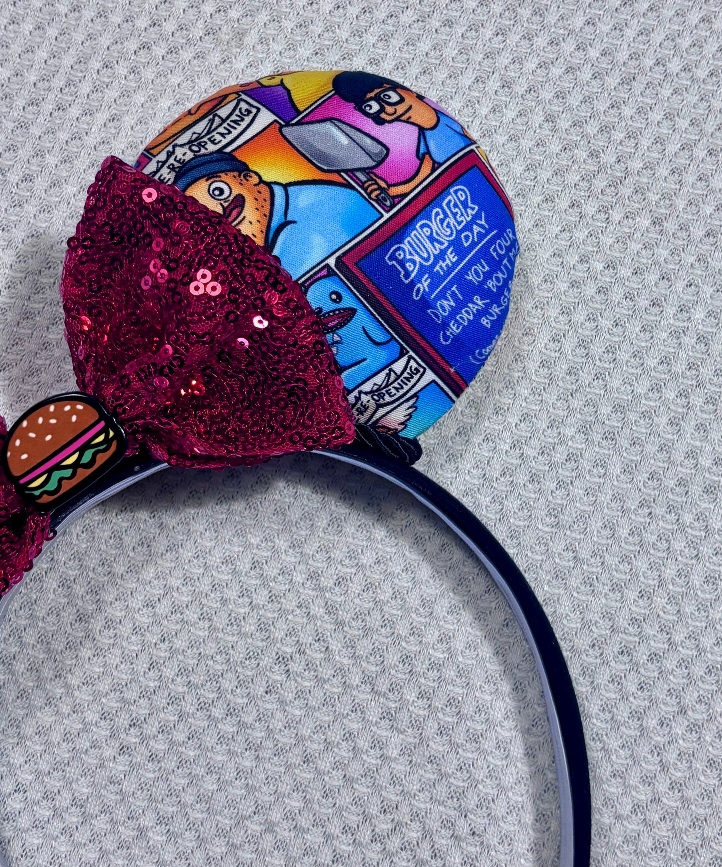 Handmade and ready to ship Belcher and friends mouse ears with the fabric on both the front and back. The headband is black universal sized and fits most. The set has a red sequin bow with a burger embellishment on the middle. Item is shown on a white background.
