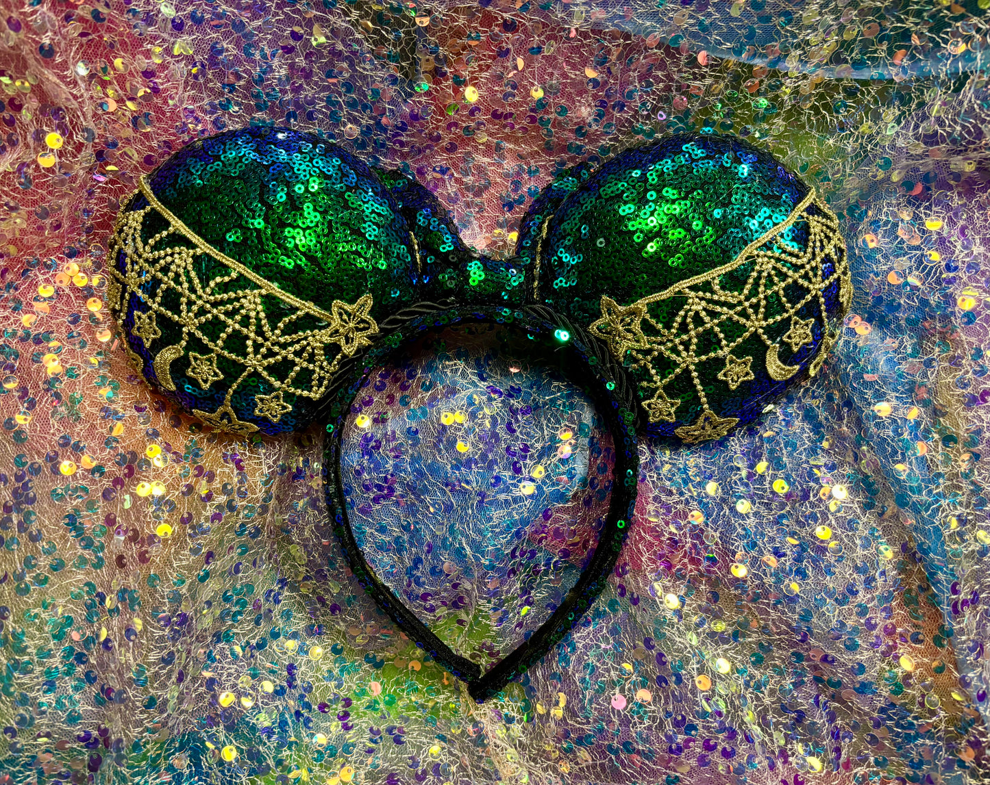 Mouse Ear headband that is a Handmade Iridescent blue and green sequins with gold sun, moon and stars attached to them. bow with star and moon patterns on a glittery background.