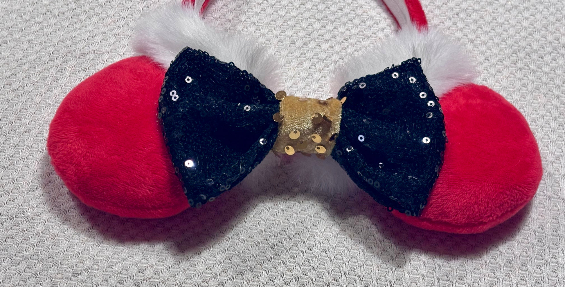 Minnie Mouse ears headband with red plush ears and black bow with gold middle and fluffy white trim on a white background