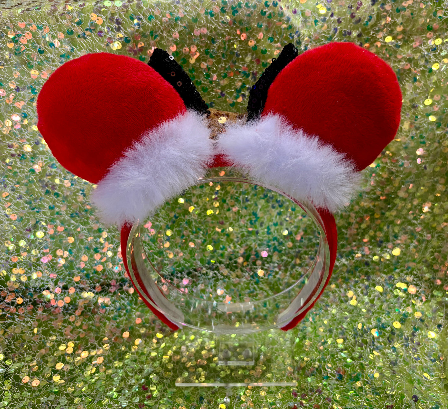 Red and white festive ears on a clear headband against a glittery background