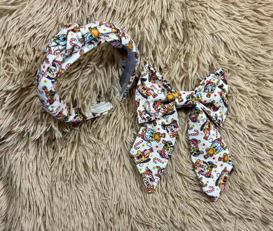 A fabric headband and matching bow accessory set with a colorful cartoon print on a white background, displayed on a beige faux fur surface.